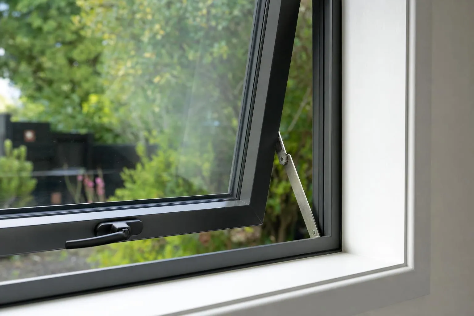 Illustrative: a charcoal aluminium awning window slightly open, showing the handle and the friction stay