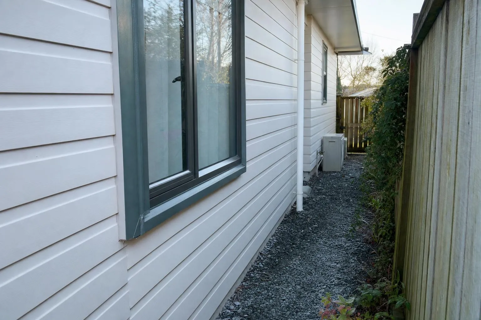 Illustrative: a new aluminium window in a weatherboard wall, with the boundary fence about a metre away across a side path