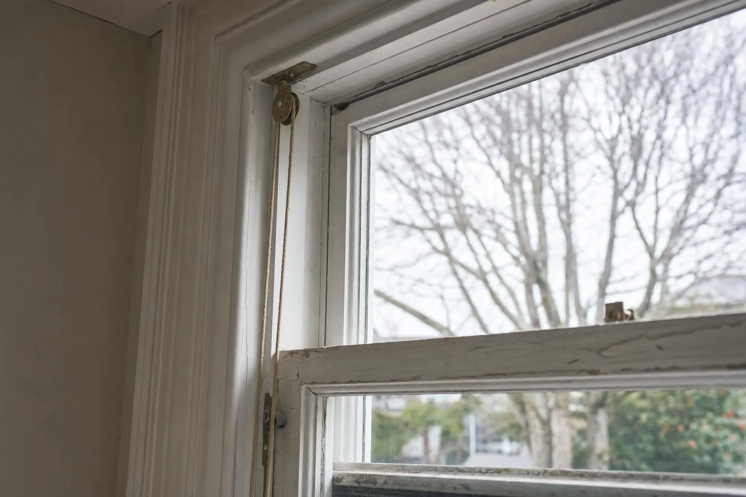 Illustrative: the sash cord and brass pulley at the top of a painted timber double-hung window