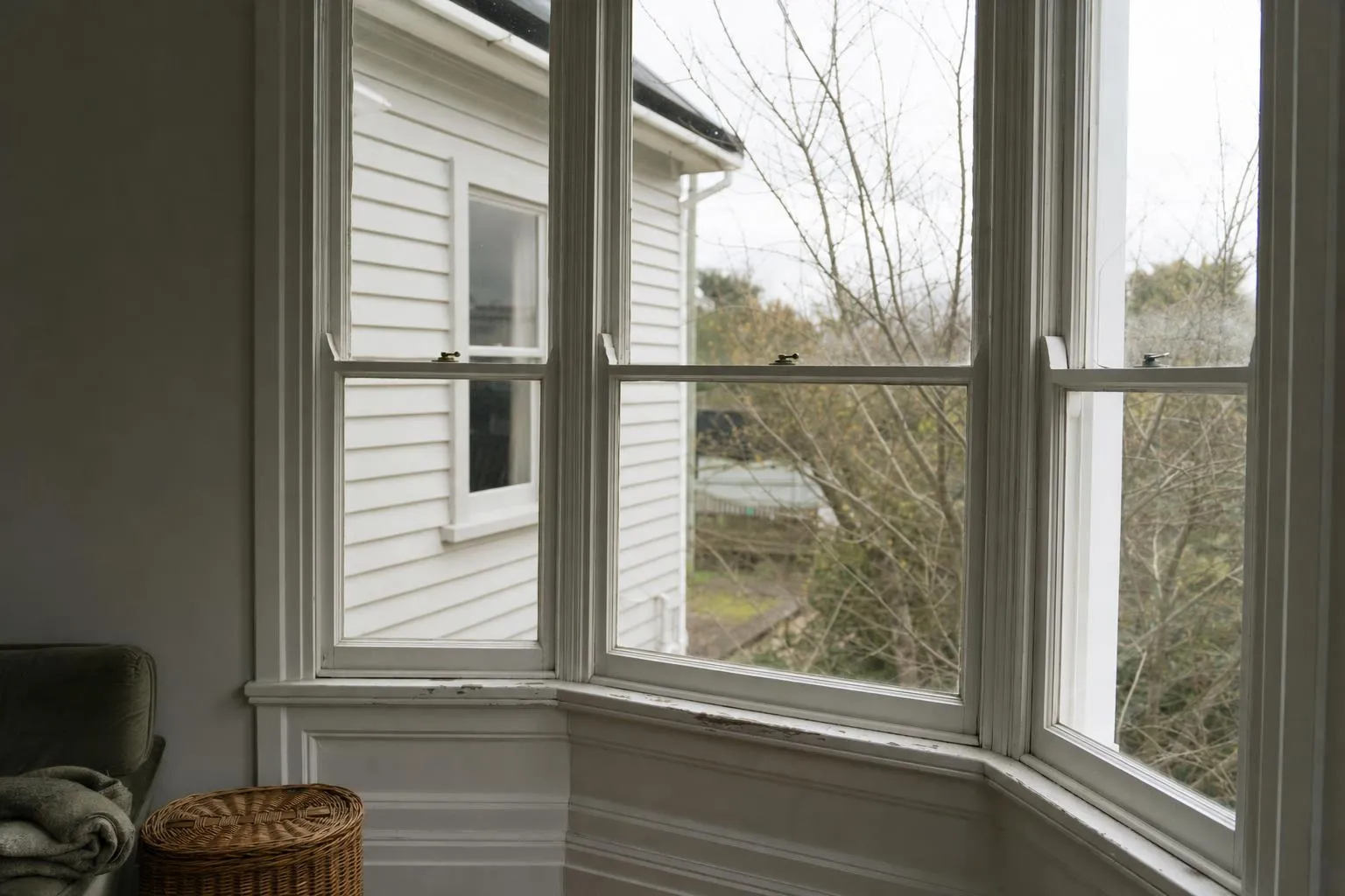 Illustrative: a painted villa bay window with worn paint on the sill and weatherboard next door