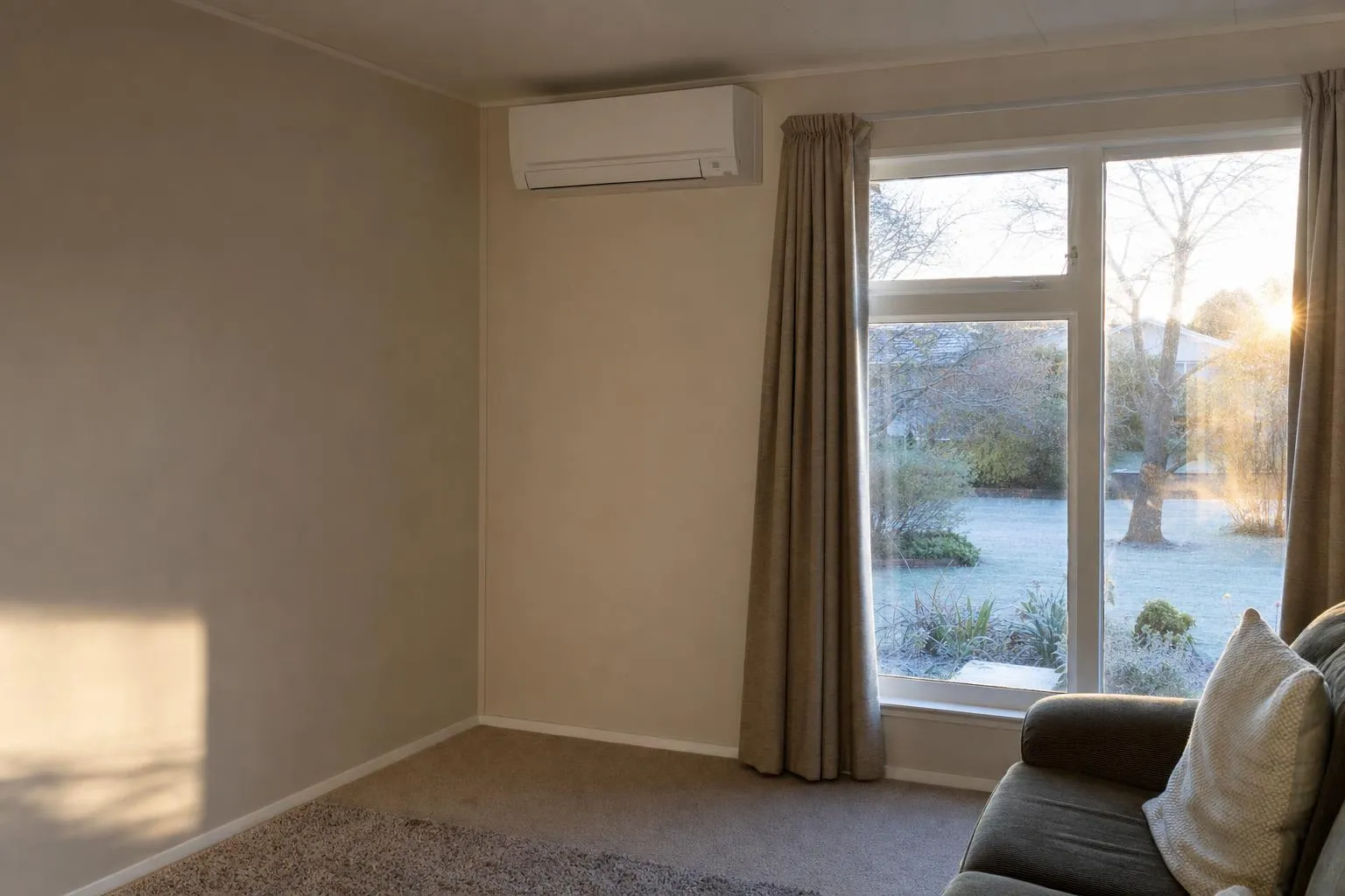 Illustrative: a plain lounge on a frosty morning with low sun through an older window and a heat pump on the wall